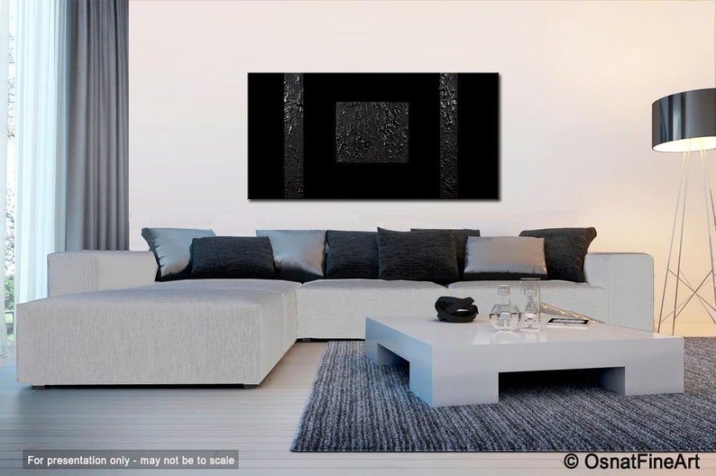 May include: A black and white abstract painting with a textured surface hangs on a white wall above a white sectional sofa with black pillows. A white coffee table sits in front of the sofa with a black rug underneath.