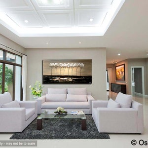 May include: A living room interior design with a large abstract painting of trees in shades of brown and white above a white sofa. Two white armchairs are placed in front of the sofa, and a glass coffee table sits between them. The room has a white ceiling with a decorative pattern and large windows.