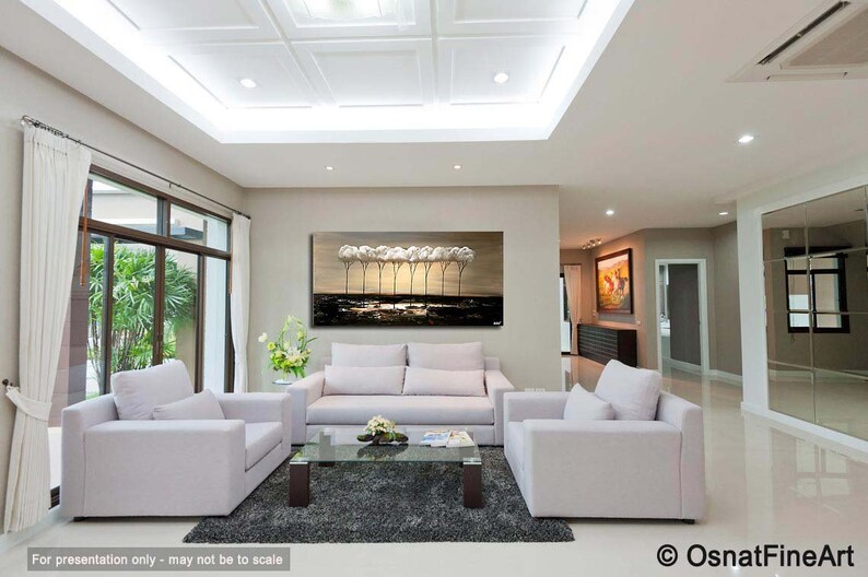 May include: A living room interior design with a large abstract painting of trees in shades of brown and white above a white sofa. Two white armchairs are placed in front of the sofa, and a glass coffee table sits between them. The room has a white ceiling with a decorative pattern and large windows.