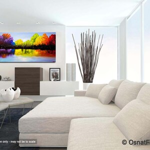 May include: Abstract painting of a colorful landscape with trees reflected in a still body of water. The painting is displayed on a wall in a modern living room setting.