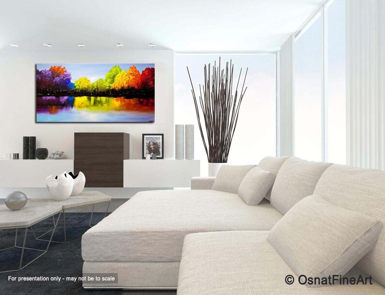 May include: Abstract painting of a colorful landscape with trees reflected in a still body of water. The painting is displayed on a wall in a modern living room setting.