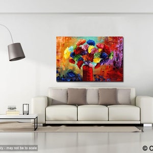 May include: An abstract painting of a bouquet of colorful flowers in a red vase. The artwork features a vibrant mix of blues, yellows, reds, and greens, creating a lively and eye-catching piece. The painting is displayed above a white sofa.