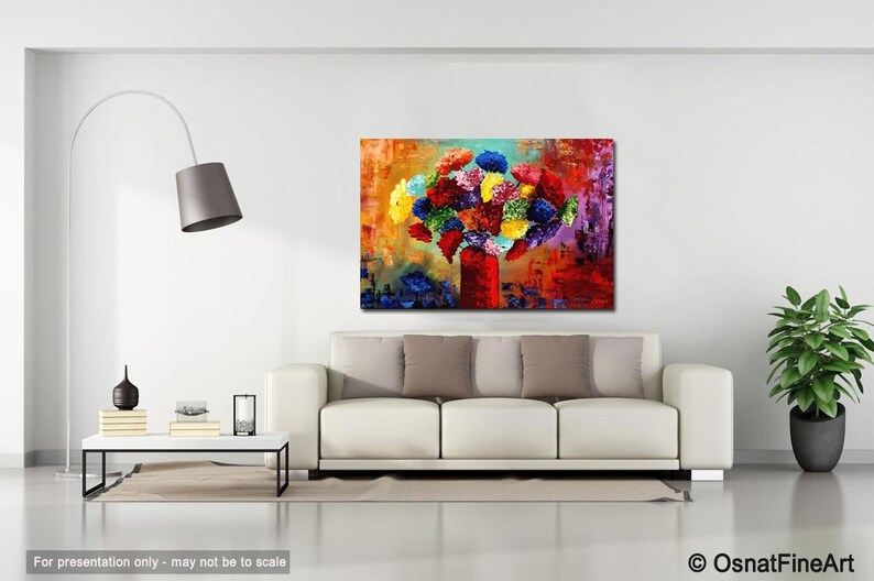 May include: An abstract painting of a bouquet of colorful flowers in a red vase. The artwork features a vibrant mix of blues, yellows, reds, and greens, creating a lively and eye-catching piece. The painting is displayed above a white sofa.
