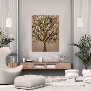 May include: A modern living room interior with a large abstract painting of a gold tree on the wall. The room features a white armchair, a white ottoman, two white side tables, and two potted plants.
