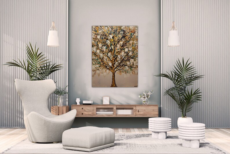May include: A modern living room interior with a large abstract painting of a gold tree on the wall. The room features a white armchair, a white ottoman, two white side tables, and two potted plants.