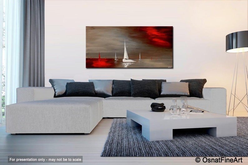 May include: Abstract painting of sailboats on a body of water with a red and gray sky. The painting is displayed on a wall above a white couch and coffee table.