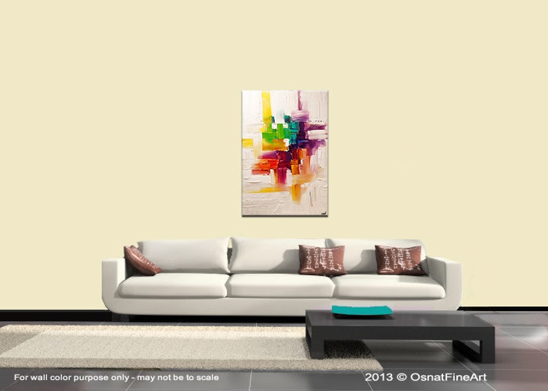 May include: Abstract painting with a white background and colorful geometric shapes in shades of red, orange, yellow, green, blue, purple, and pink. The painting is displayed on a white wall above a white couch with brown pillows.