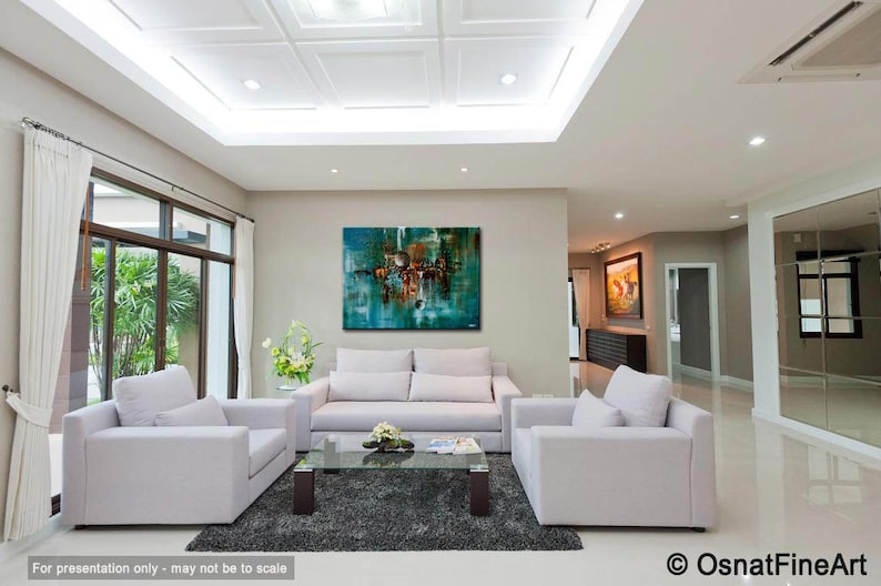 May include: Abstract painting in shades of teal, brown, and white, hanging on a wall in a living room with white couches and a coffee table. The painting is framed and has a modern style.