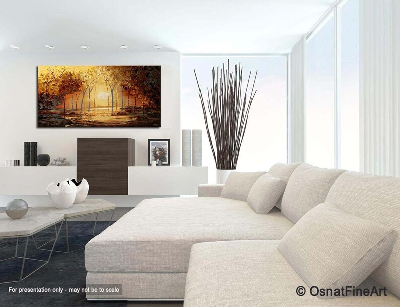 May include: A painting of a forest scene with trees in shades of brown and yellow. The trees are reflected in a still body of water in the foreground. The painting is displayed on a white wall above a white couch with pillows.