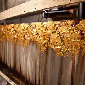 May include: Abstract painting with gold leaf accents on a canvas. The painting features a textured, layered look with shades of brown, gold, and white.