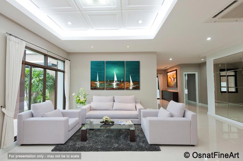 May include: A three-piece abstract painting of sailboats on a teal and blue ocean with a sunset in the background. The painting is hanging on a wall in a living room with white furniture.