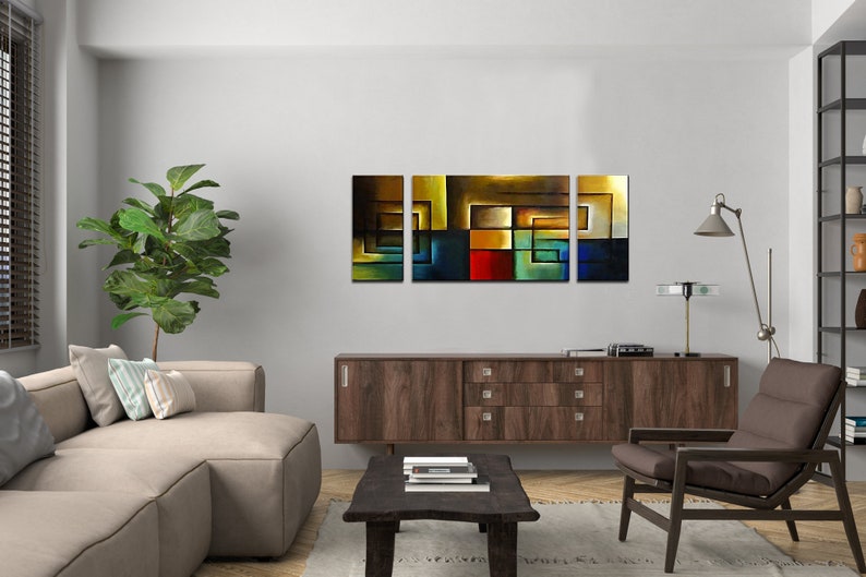 May include: A three-piece abstract art print set featuring geometric shapes in shades of blue, green, red, yellow, and brown. The prints are framed and hung on a white wall above a brown wooden cabinet.