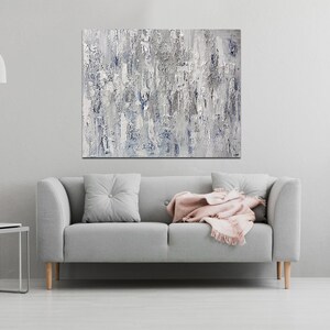 May include: A gray sofa with a pink throw blanket and a gray pillow in a living room with a white wall and a painting above the sofa.