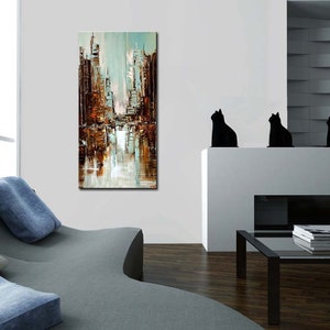 May include: Abstract painting of a city skyline in shades of brown, blue, and white. The painting is hanging on a white wall in a modern living room.