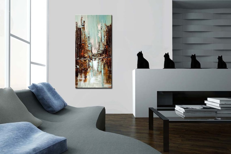 May include: Abstract painting of a city skyline in shades of brown, blue, and white. The painting is hanging on a white wall in a modern living room.