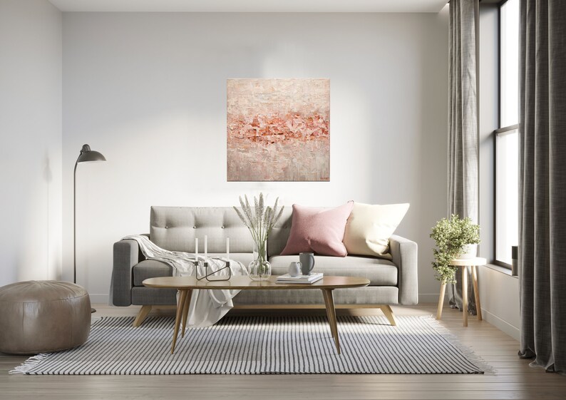 May include: A living room interior with a gray sofa, a coffee table, a rug, a floor lamp, a potted plant, and a painting on the wall. The painting is abstract and features a pink and white color scheme.