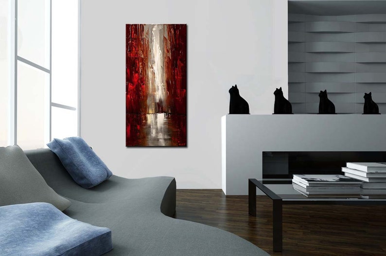 May include: Abstract painting with red, white, and gray colors. The painting depicts a city scene with tall buildings and a reflective surface. The painting is hanging on a white wall in a living room setting.