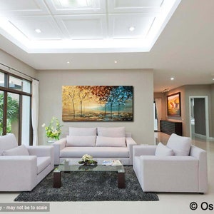 May include: A living room interior design featuring a large abstract painting of trees in shades of gold, red, blue, and green. The painting is hung on a wall above a white sofa and two white armchairs. The room has a white ceiling with recessed lighting and a large window with white curtains.