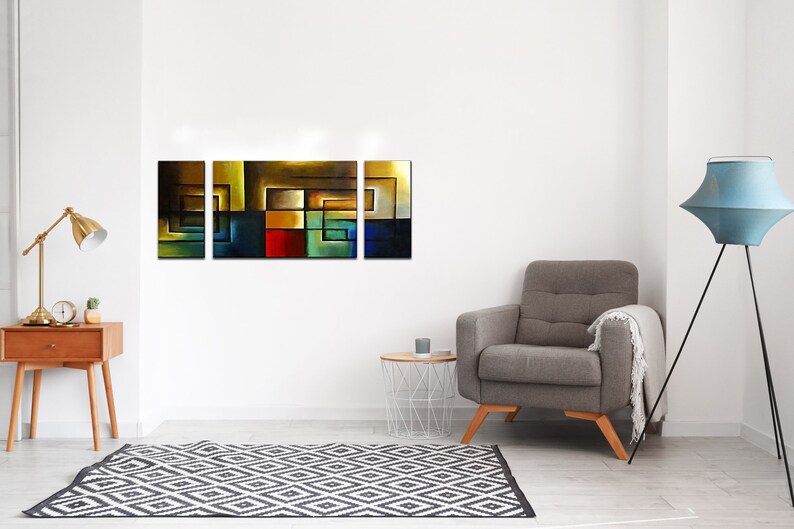 May include: A four-piece abstract art print set featuring geometric shapes in shades of blue, green, yellow, red, and brown. The prints are arranged horizontally on a white wall above a gray armchair.