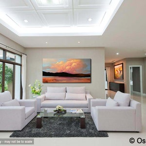 May include: A living room interior with a large abstract landscape painting on the wall. The painting features a pink and orange cloud formation over a body of water. The room is furnished with a white sofa, two armchairs, and a glass coffee table.