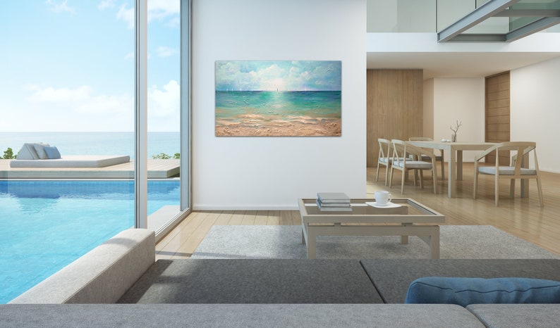 May include: A painting of a seascape with a sailboat in the distance. The painting is framed and hanging on a white wall in a modern living room. The room has a large window with a view of a swimming pool and the ocean.
