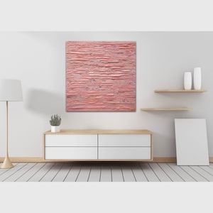 May include: A pink abstract painting with horizontal brushstrokes hangs on a white wall above a white dresser with four drawers. The painting is in a modern living room setting with a white lamp and a small potted plant on the dresser.