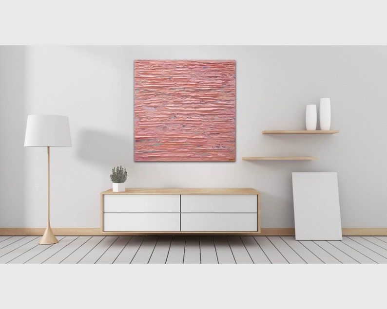 May include: A pink abstract painting with horizontal brushstrokes hangs on a white wall above a white dresser with four drawers. The painting is in a modern living room setting with a white lamp and a small potted plant on the dresser.