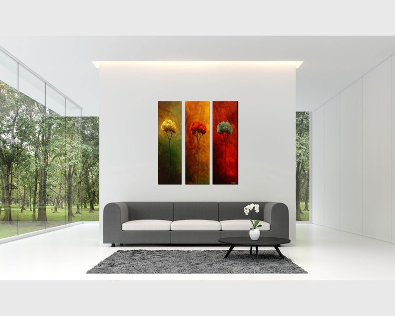May include: Three abstract paintings of trees in a modern living room with a gray sofa and a white orchid plant on a black coffee table.