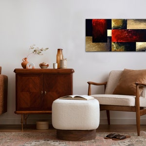 May include: Abstract painting with geometric shapes in shades of red, gold, and black. The painting is hanging on a white wall in a living room setting with furniture and decor.