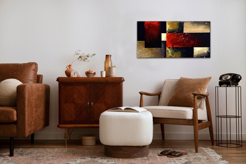 May include: Abstract painting with geometric shapes in shades of red, gold, and black. The painting is hanging on a white wall in a living room setting with furniture and decor.