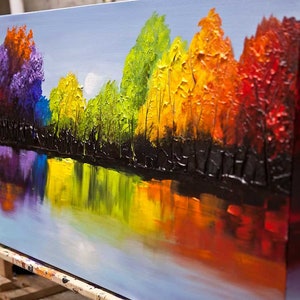 May include: A colorful abstract painting of a forest reflected in a lake. The trees are painted in shades of purple, blue, green, yellow, orange, and red. The lake is a light blue with reflections of the trees.
