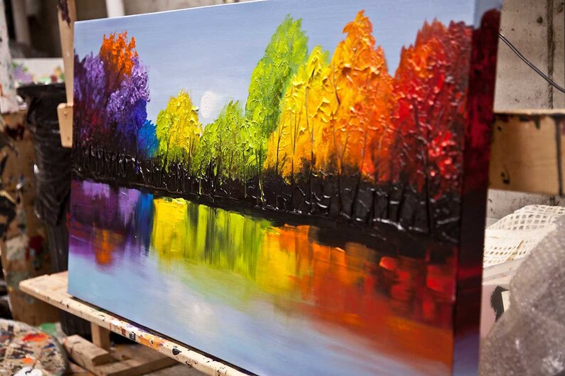 May include: A colorful abstract painting of a forest reflected in a lake. The trees are painted in shades of purple, blue, green, yellow, orange, and red. The lake is a light blue with reflections of the trees.