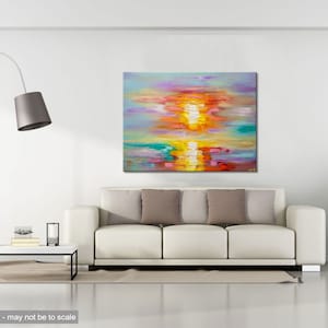 May include: Abstract painting of a sunset over water with vibrant colors of pink, orange, yellow, blue, and green. The painting is displayed on a white wall above a white sofa with gray pillows.