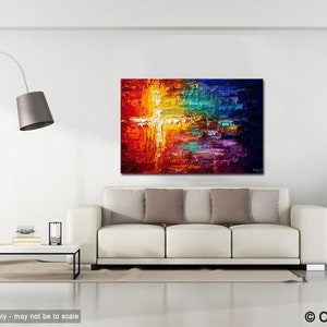 May include: Abstract painting with a white cross in the center, surrounded by vibrant colors like red, orange, yellow, green, blue, and purple. The painting is displayed on a white wall above a white sofa with pillows.