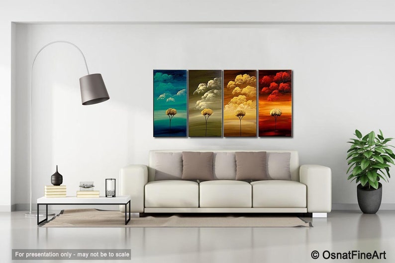 May include: A set of four abstract paintings depicting stylized trees in different colors. The paintings are arranged in a row on a white wall above a white sofa with beige pillows. The paintings are in shades of blue, green, yellow, and red.
