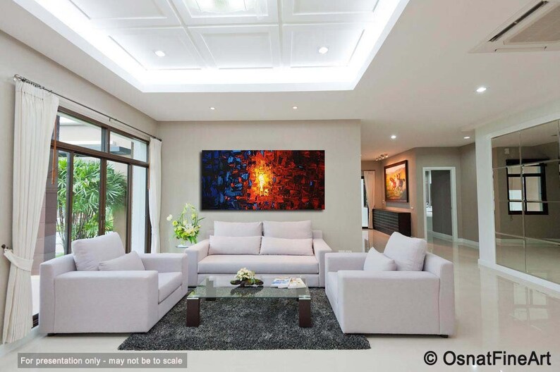 May include: Abstract painting in shades of blue, orange, and yellow. The painting is displayed on a wall in a living room with white couches and a coffee table.