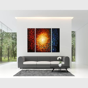 May include: A three-piece abstract painting with a bright yellow center surrounded by red, orange, and blue hues. The painting is displayed on a white wall above a gray sofa in a modern living room.