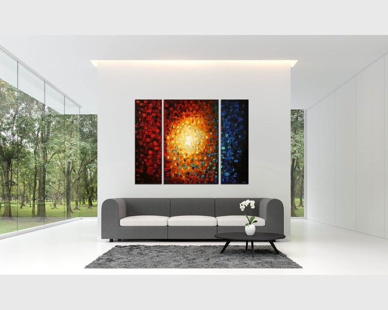 May include: A three-piece abstract painting with a bright yellow center surrounded by red, orange, and blue hues. The painting is displayed on a white wall above a gray sofa in a modern living room.