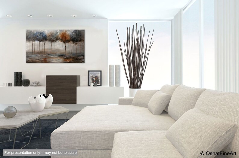 May include: A white sectional sofa with multiple pillows in a modern living room. The sofa is in front of a large window with white curtains. A painting of trees in shades of blue, brown, and gray hangs on the wall above a brown entertainment center.