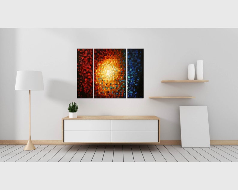May include: A three-piece abstract painting with a central panel featuring a bright yellow sunburst surrounded by red, orange, and blue hues. The side panels are red and blue.