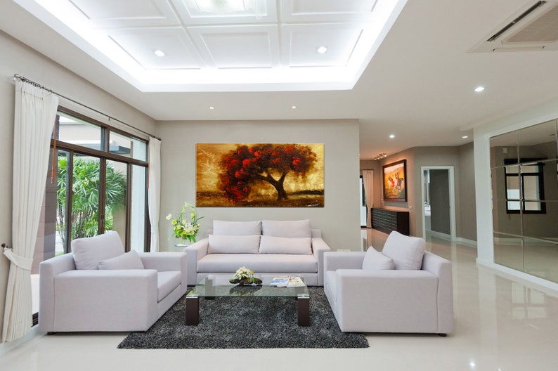 May include: A living room interior with white couches and a coffee table. A large painting of a red tree with a golden background hangs on the wall.