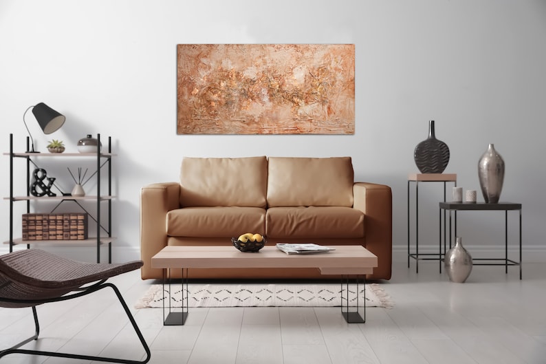 May include: An abstract painting with a textured surface in shades of beige, brown, and gold hangs above a tan leather sofa. The living room features a wooden coffee table, black metal side tables, and decorative vases.