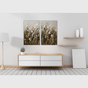 May include: A white, wooden, four-drawer dresser with a white, framed painting of a field of white flowers and brown grass hanging above it.