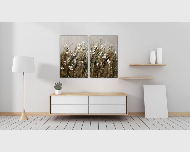 May include: A white, wooden, four-drawer dresser with a white, framed painting of a field of white flowers and brown grass hanging above it.