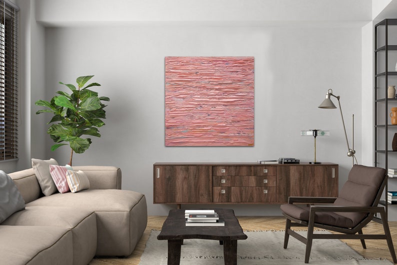 May include: A pink abstract painting with horizontal lines and a textured surface hangs on a white wall above a brown wooden cabinet. The painting is in a modern living room setting with a sofa, armchair, and coffee table.