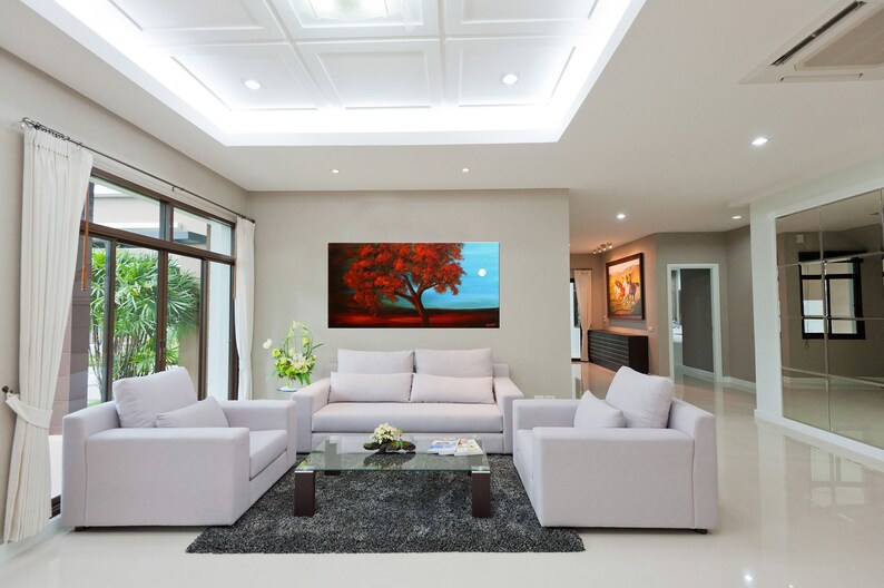 May include: A living room interior with white couches and a coffee table. A large painting of a red tree with a full moon in the background hangs on the wall.