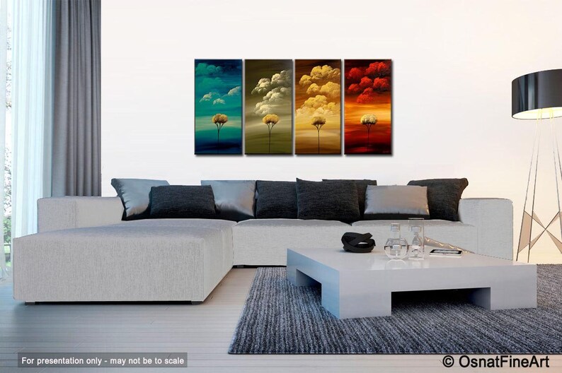 May include: A four-panel abstract painting depicting a stylized tree with a yellow trunk and green, blue, yellow, and red foliage against a background of clouds. The painting is displayed in a living room setting with a white sofa, a white coffee table, and a black floor lamp.