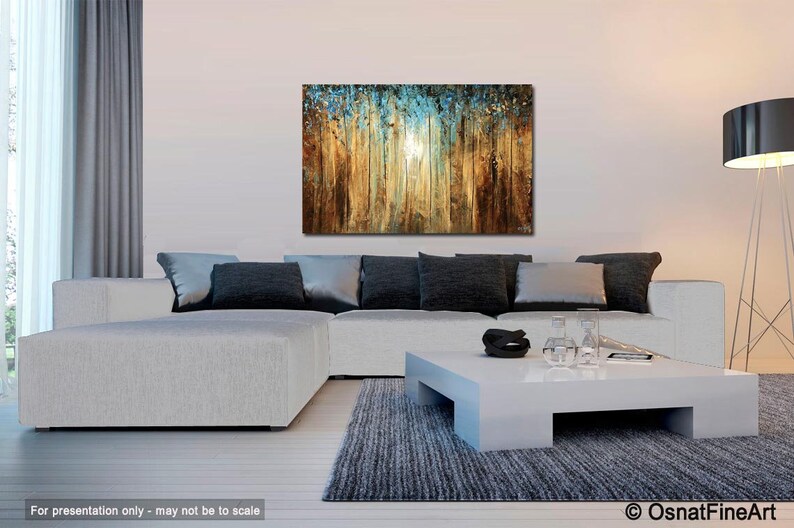 May include: Abstract painting of a forest scene with a blue and gold color scheme. The painting is hanging on a wall above a white sectional sofa and a white coffee table.