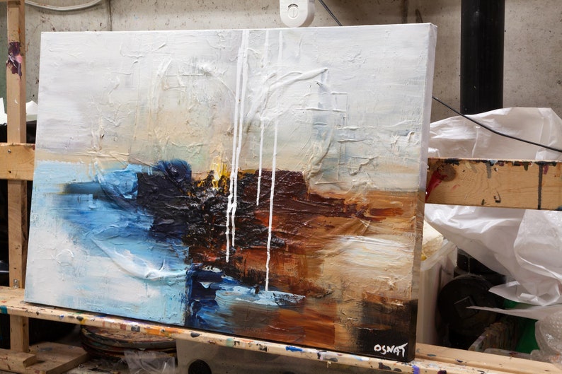 May include: Abstract painting on canvas with white, blue, brown, and black paint. The paint is applied in thick layers and has a textured surface. The painting is signed "OSNAT" in the lower right corner.