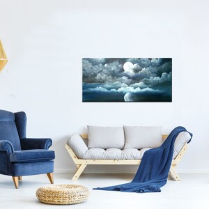 May include: A painting of a full moon shining through dark clouds in a night sky. The moon is white and the clouds are dark gray. The sky is a deep blue. The painting is framed and hanging on a white wall.